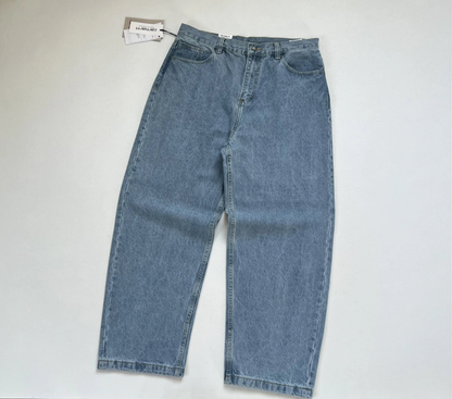 A pair of light baggy vintage Carhartt blue denim jeans laid flat on a light gray background, with a small hangtag attached near the waistband.