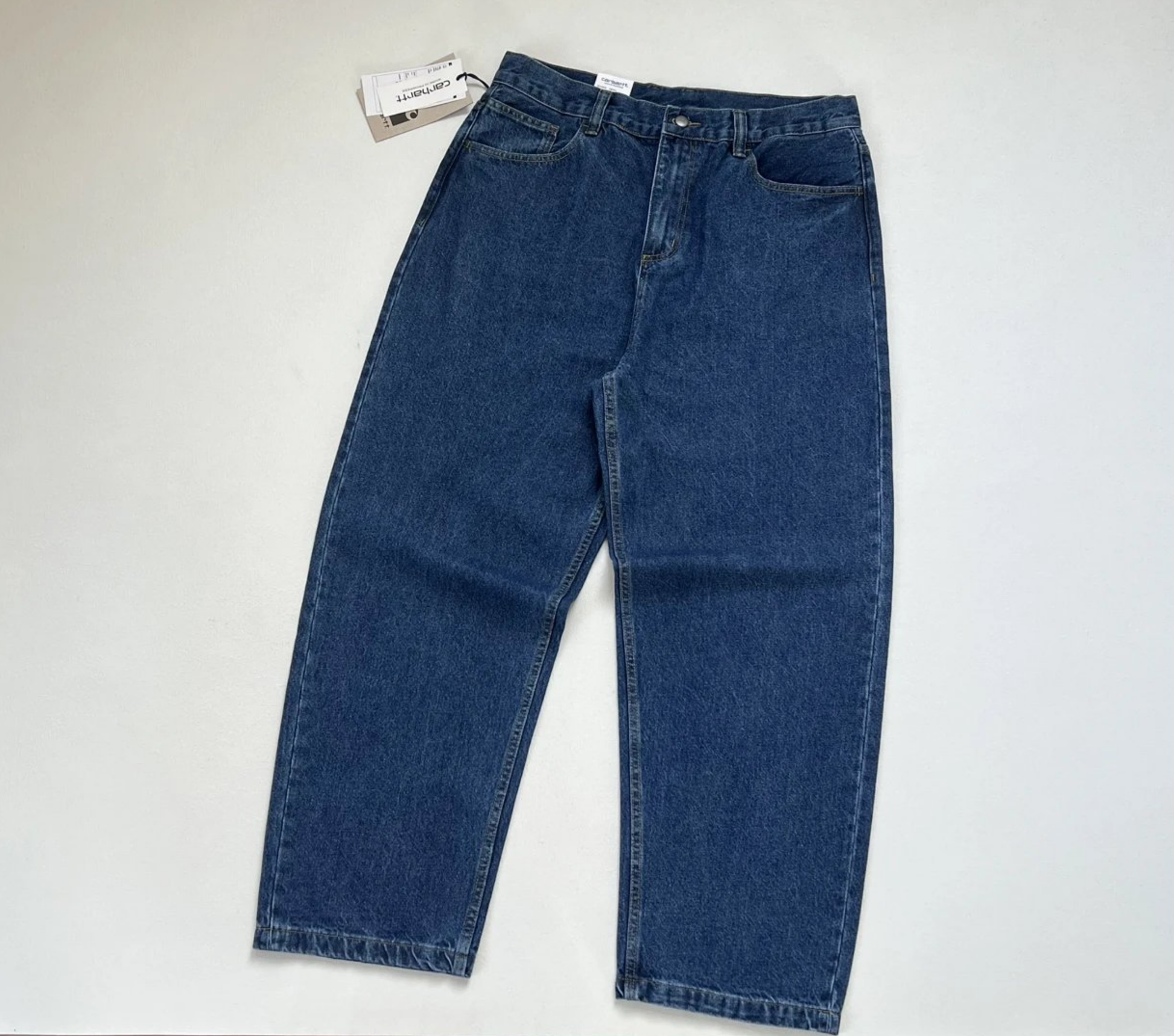 A pair of baggy vintage Carhartt dark blue denim jeans laid flat on a light gray background, with a white brand tag attached near the waistband.