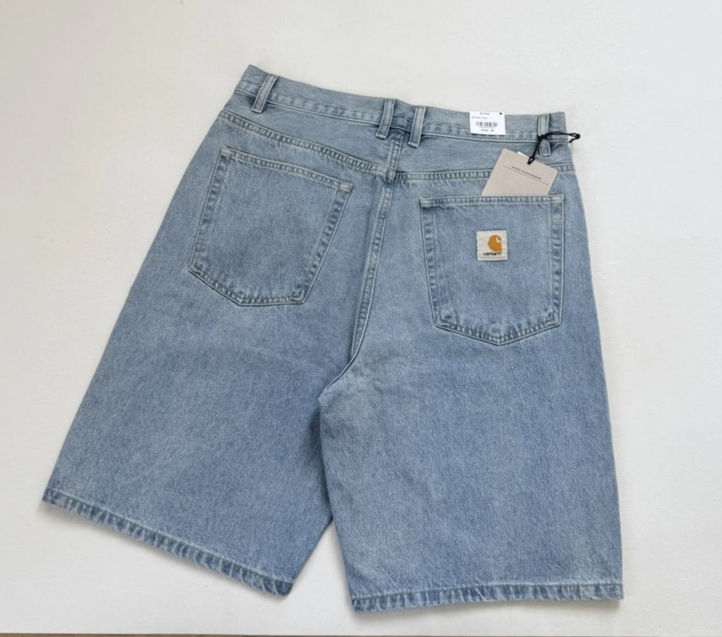 Light blue denim shorts with a faded wash, featuring two back pockets and a visible Carhartt logo patch on the right pocket, laid flat on a white background.