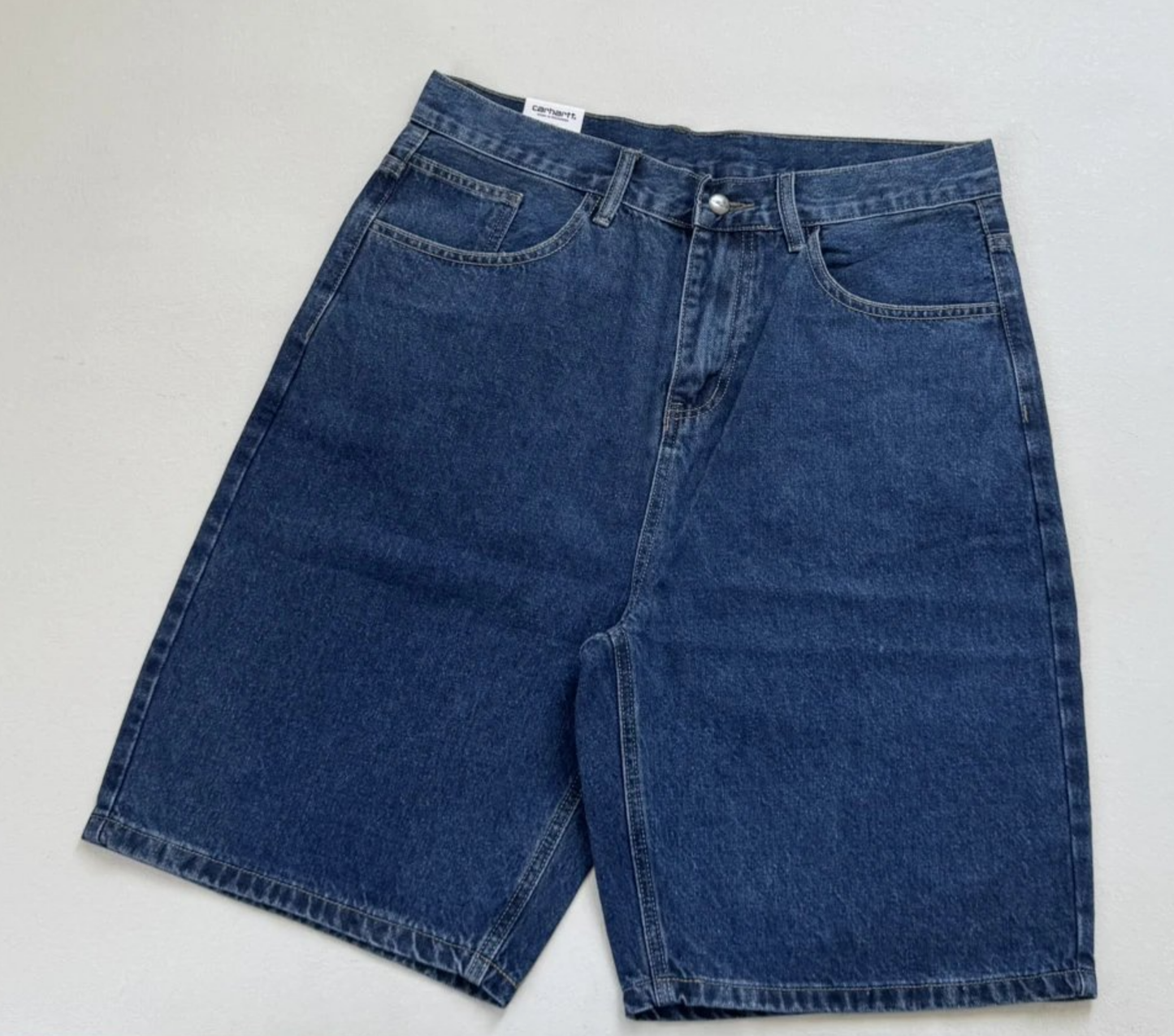 A pair of dark blue carhartt denim shorts laid flat on a light gray background. Navy baggy jorts for men, Y2K Pants